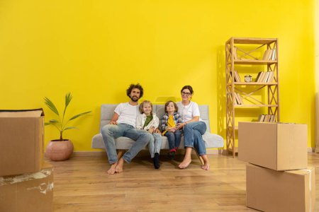 Photo for In large modern living room happy family parents and two kids moving in a new home they take a sit on the sofa and enjoy the time together. Family - Royalty Free Image