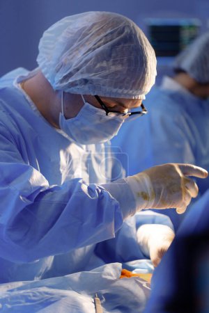 Téléchargez les photos : Plan rapproché du chirurgien portant des lunettes et se concentrant sur l'exécution d'une opération dans une salle médicale. - en image libre de droit