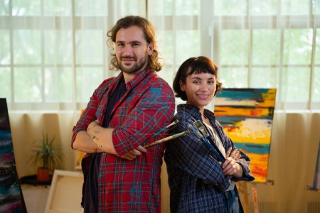 Foto de Atractivo y guapo dos artista posando delante de la cámara en el estudio de arte que sostiene los pinceles de pintura y cruzar las manos sonriendo lindo. Pintura - Imagen libre de derechos