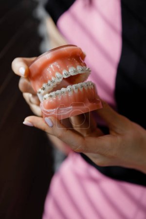 Téléchargez les photos : Le dentiste vous montre comment vous brosser les dents avec une brosse à dents sur la disposition de la mâchoire. Gros plan des médecins mains dans les gants au travail. Modèle de dents pour démonstration. Dentiste - en image libre de droit