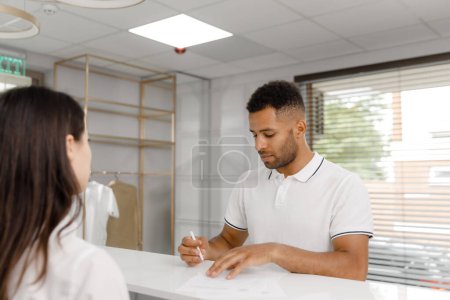 Photo for Charismatic man closeup to the camera at reception desk in the modern medical clinic signed some blank information after he goes to the doctors office. - Royalty Free Image