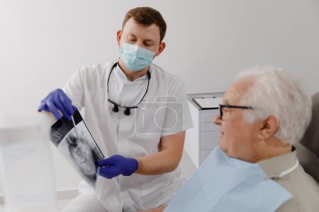 Paciente anciano bien parecido tiene una cita en el dentista que se sienta en la silla del dentista y discutir con el médico los problemas de la caries. Dentista