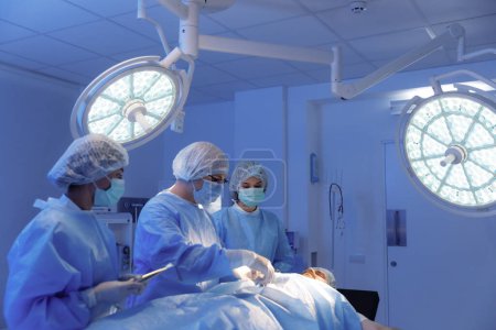 Téléchargez les photos : Un chirurgien utilise une boule de coton trempée dans un liquide sombre pour préparer son patient à l'opération, le chirurgien et ses deux assistants portent un équipement chirurgical complet. - en image libre de droit