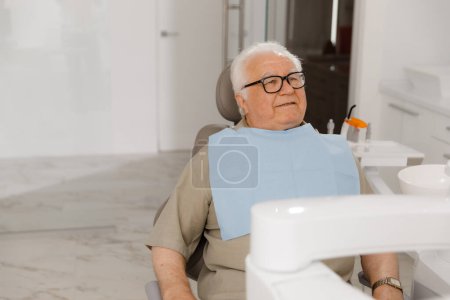 Téléchargez les photos : Concept d'affaires de dentisterie devant la caméra vieil homme patient posant devant la caméra au cabinet de dentiste il sourit mignon et regardant droit. Dentiste - en image libre de droit