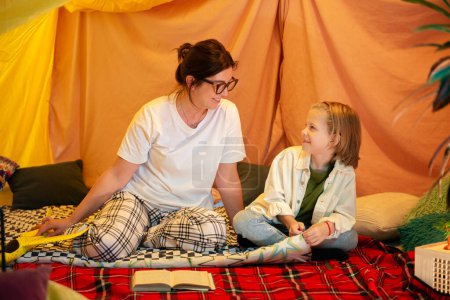 Photo for A further away shot of a mother bonding with her son as she reads out a book to him and seems to enjoy herself she is wearing comfortable clothes inside the blanket fort. Family - Royalty Free Image