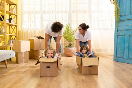 Photo for Great time for a cute charismatic kids they have a ride with boxes after they moving in a new home their parents pushing the boxes through the floor in the living room. Family - Royalty Free Image