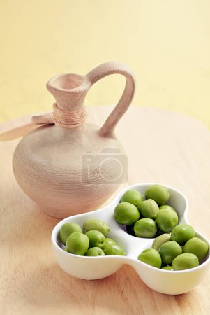 Olives in white playe with a jar on the wooden plate