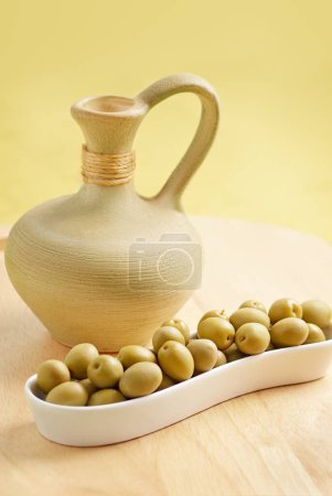 Olives in white playe with a clay jar on the wooden plate