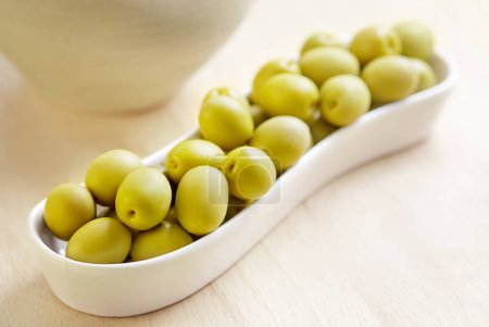 Grüne Oliven in weißem Teller auf Holzbrett