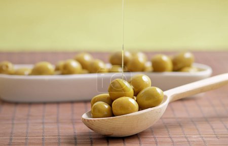 Foto de Aceite de oliva vertido sobre aceitunas verdes en cuchara de madera - Imagen libre de derechos