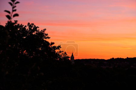 Silhouette of village and forest against sunset sky