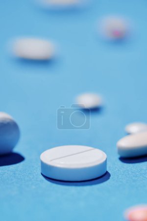 Téléchargez les photos : Médecine et concept de drogue. Gros plan de la pilule blanche sur fond bleu avec différents comprimés sur elle hors foyer. - en image libre de droit