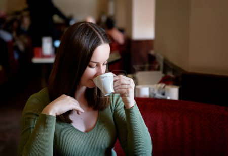 Photo for Drinking coffee. Pretty young woman holding cup of beverage while sitting at cafe. - Royalty Free Image