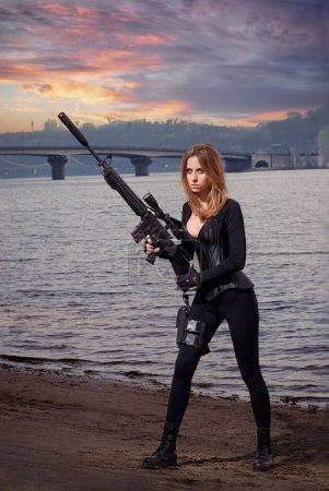 Photo for Portrait of young beautiful woman with a assault rifle gun on the river bank - Royalty Free Image