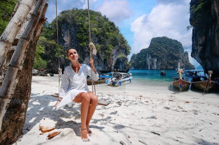 Téléchargez les photos : Détendez-vous. Jeune femme balançant sur la planche à thé près de la mer avec des bateaux de pêche à queue longue en Thaïlande. - en image libre de droit