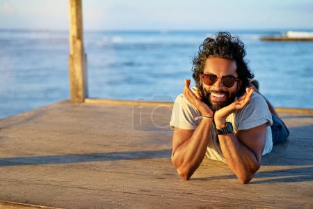 Téléchargez les photos : Amusant et joyeux. Portrait extérieur de jeune homme africain heureux reposant sur le pont près de la mer. - en image libre de droit