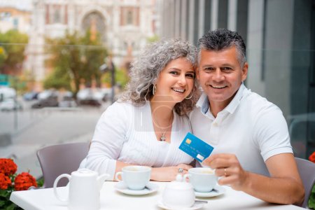 Foto de Paga la cuenta. Atractiva pareja familiar de ancianos con tarjeta de crédito de plástico mientras se encuentra en la cafetería de la acera. - Imagen libre de derechos
