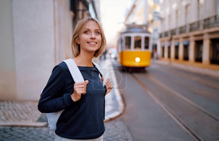 Téléchargez les photos : Voyager au Portugal. Joyeux jeune femme avec sac à dos marchant dans les rues de Lisbonne. - en image libre de droit