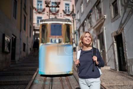 Téléchargez les photos : Voyager au Portugal. Joyeux jeune femme avec sac à dos marchant dans les rues de Lisbonne. - en image libre de droit