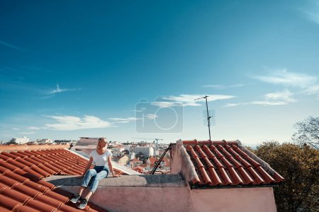 Photo for Traveling by Portugal. Young traveling woman enjoying old town Lisbon view on red tiled roof. - Royalty Free Image
