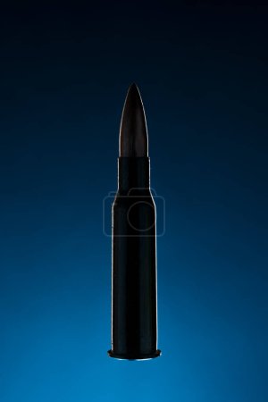 Photo for Rifle bullet long cartridge on blue background. Army or hunting weapon shot object, violence and danger symbol. - Royalty Free Image