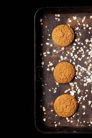 Photo for Craft and rustic four oatmeal cookies. Dark food aesthetics, black background with several oat flakes. - Royalty Free Image