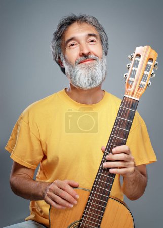 Hombre envejecido con una guitarra sobre fondo gris
