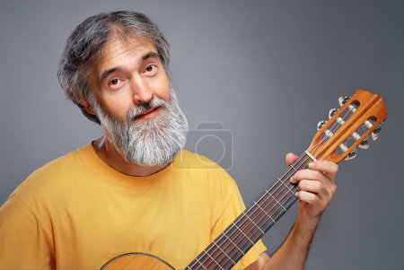 Homme âgé avec une guitare sur fond gris

