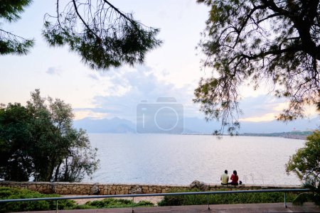Photo for Friends sitting on the brick fence while looking at sunset on the sea. Antalya, Turkey. - Royalty Free Image