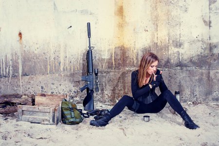 Foto de Una señora rudo en un traje negro fuma un cigarrillo mientras está sentada cerca de su equipo de combate. - Imagen libre de derechos
