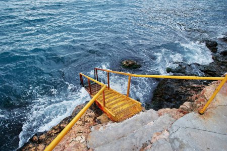 Téléchargez les photos : Escaliers jaunes se dirigeant vers la plage océanique alors que la mousse de mer et les vagues s'enfoncent. - en image libre de droit