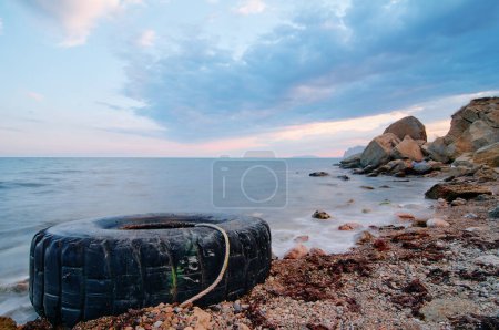 Foto de Neumáticos viejos en la orilla. Agua y contaminación de la costa neumáticos de coches en la playa de arena. - Imagen libre de derechos
