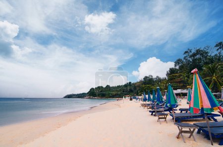Foto de Vacaciones tropicales. Hermosa playa de arena con tumbonas y sombrillas. Cielo nublado. - Imagen libre de derechos