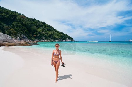 Téléchargez les photos : Vacances tropicales. Jeune femme marchant sur la plage de la mer bleue tropicale avec tuba à la journée ensoleillée. - en image libre de droit