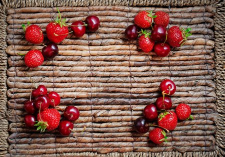 Strawberries, cherries frame on the rustic surface.