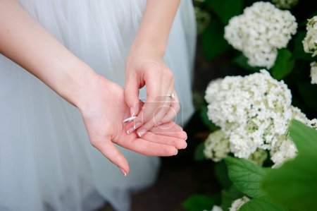 Foto de Concepto de anillo de boda. Hermosas manos de novia jugando con magnífico anillo cerca de flores de flor blanca. - Imagen libre de derechos
