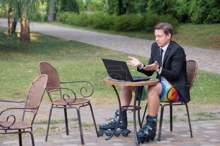 Foto de Trabajar y relajarse. Hombre de negocios vestido de traje, pantalones cortos y rodillos que trabajan con el ordenador portátil en la cafetería al aire libre - Imagen libre de derechos