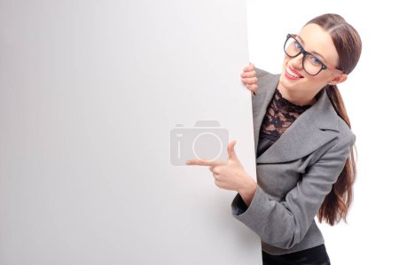 Photo for Happy smiling young business woman wearing glasses showing blank signboard pointing with her finger, isolated on white background - Royalty Free Image