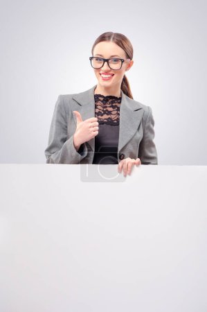 Foto de Mujer de negocios retrato aislado. Sonriente joven caucásica sosteniendo un gran tablero en blanco y mostrando el pulgar hacia arriba. Cara de emoción. - Imagen libre de derechos