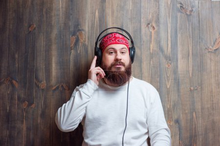 In the rhythm of my music. Relaxed young bearded man in headphones leaning on wooden wall and listening to the music.