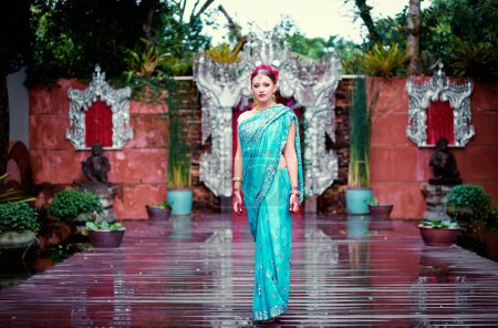 Téléchargez les photos : Belle jeune femme caucasienne en vêtements indiens traditionnels avec maquillage nuptial et bijoux. Bollywood danseuse à Sari et henné sur les mains marchant sur le jardin du temple. - en image libre de droit