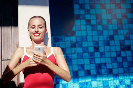 Foto de Vacaciones y tecnología. Retrato colorido de una mujer joven y bonita usando un teléfono inteligente en la piscina. - Imagen libre de derechos