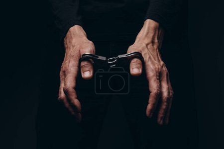 Ein Mann in Handschellen vor schwarzem Hintergrund.