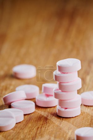 Foto de Concepto de baile de drogas. La torre de pequeñas píldoras de color rosa sobre fondo de madera con un montón de tabletas alrededor. - Imagen libre de derechos