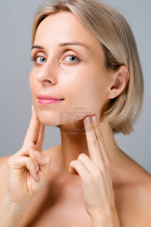 Skin care. Blonde woman with beauty face facial massage. No makeup. Grey background.
