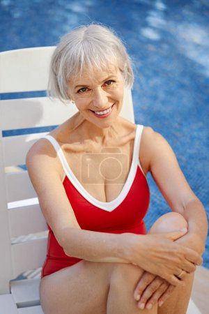 Photo for Happy vacation. Senior woman in red swimwear on the sunlounger near the swimming pool. - Royalty Free Image