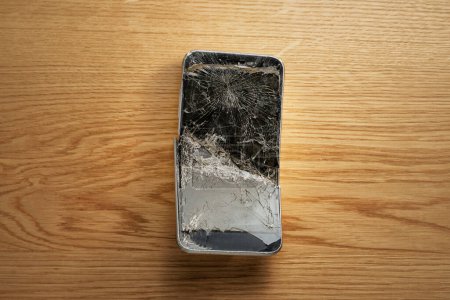 Téléchargez les photos : Smartphone mobile avec écran cassé sur fond en bois. - en image libre de droit