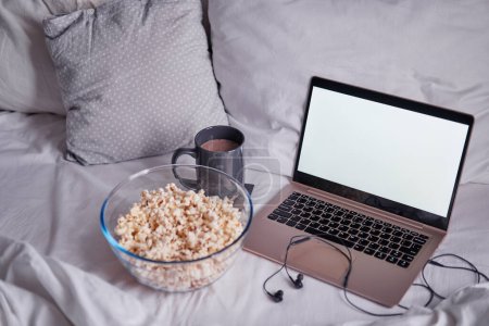 Téléchargez les photos : Regarder un film à la maison. Popcorn dans le bol et ordinateur portable au lit. Concept de divertissement. - en image libre de droit