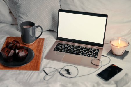 Foto de Desayuno en la cama: una bandeja de madera con granola y una taza de cacao con un ordenador portátil en el fondo. - Imagen libre de derechos