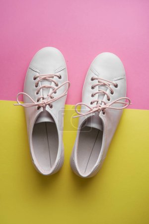 Photo for Pair of white gumshoes on pink-yellowl background. - Royalty Free Image
